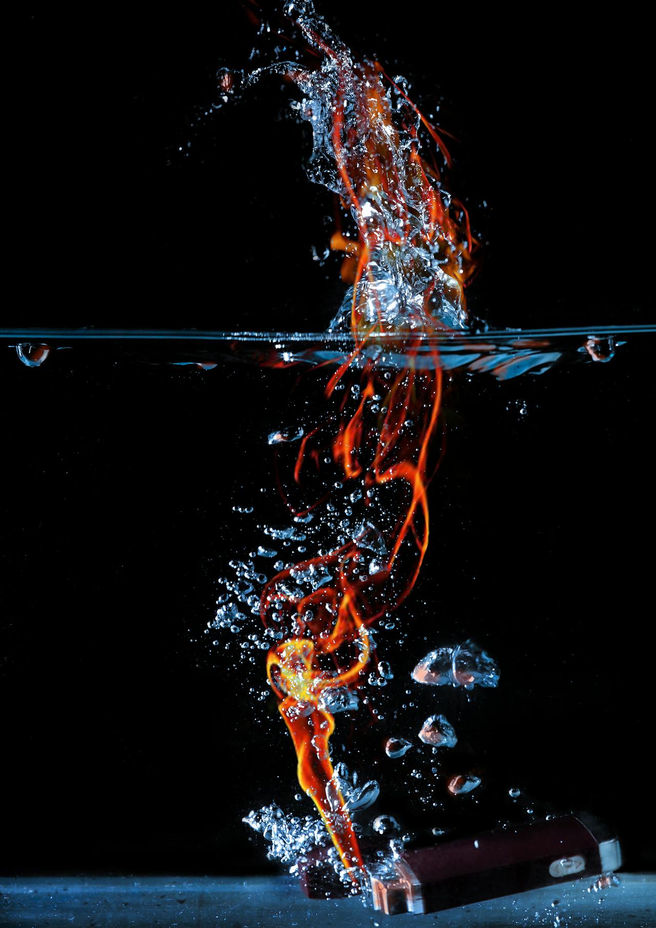 A piece of metal creates fire under water; the columnnn of flame is surrounded by bubbles, all against a black background