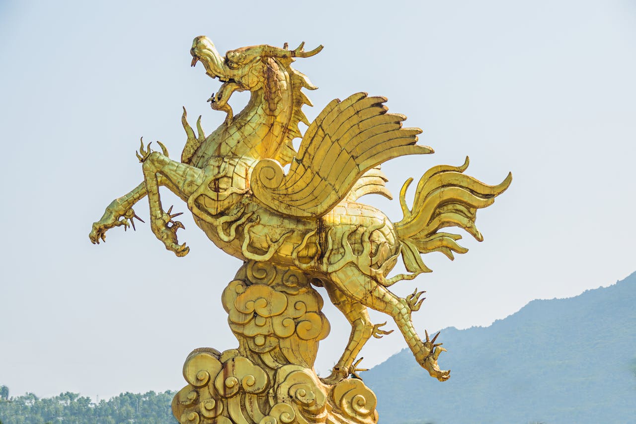 A gold statue of a very horse-looking Asian dragon with a rooster tail probably on a rooftop against a misty mountain scape